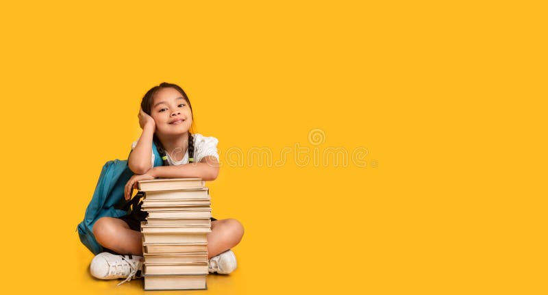 Asian Elementary Student Girl Sitting At Books Stack, Yellow Background royalty free stock photos