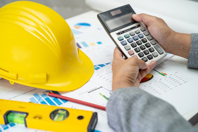 Asian engineer with architectural house plan project blueprint, graph and yellow helmet and engineering construction tools stock image