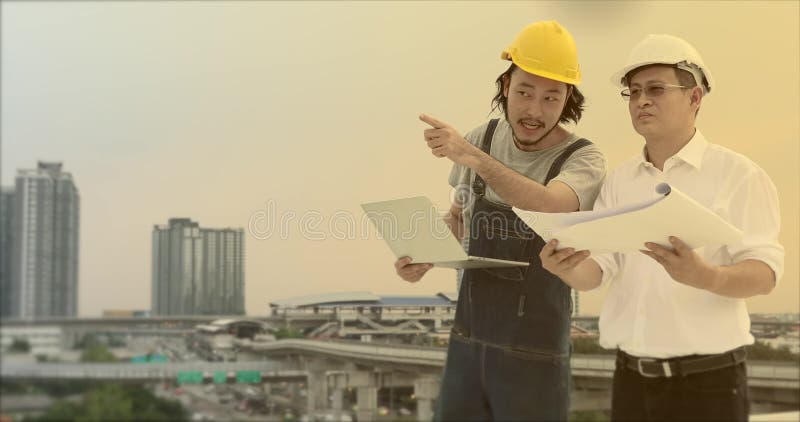 Asian engineers standing on rooftop, the young using notebook to explain his work to the old stock footage