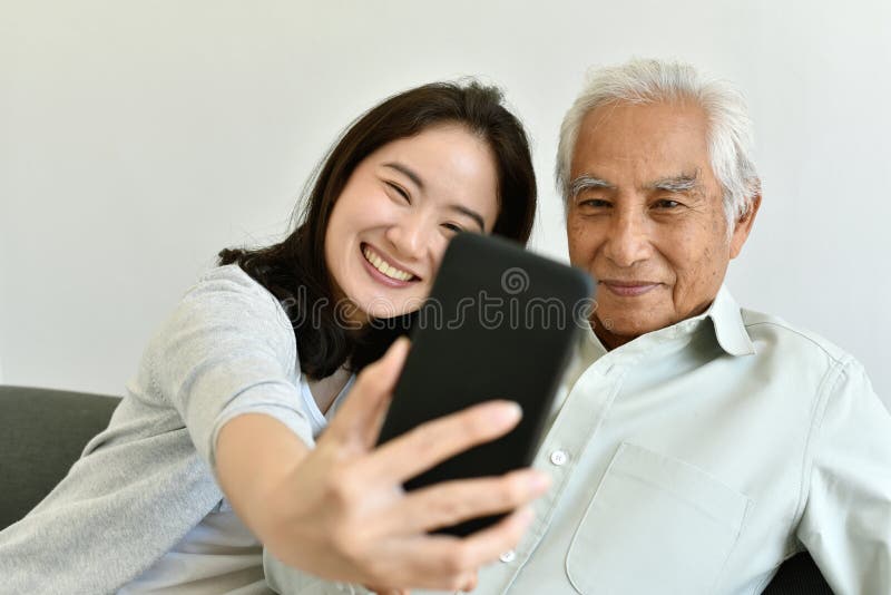 Asian family relationship, Daughter and elderly father using smartphone for selfie together. stock photo