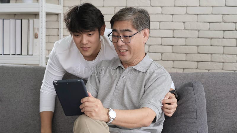 Asian father and son waving hands looking at camera, make video call with digital tablet