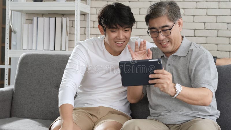 Asian father and son waving hands looking at camera, make video call with digital tablet