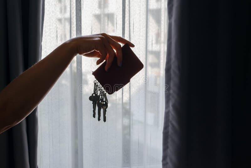 Asian female hand holding leather key holder with backlight and building behind curtains background