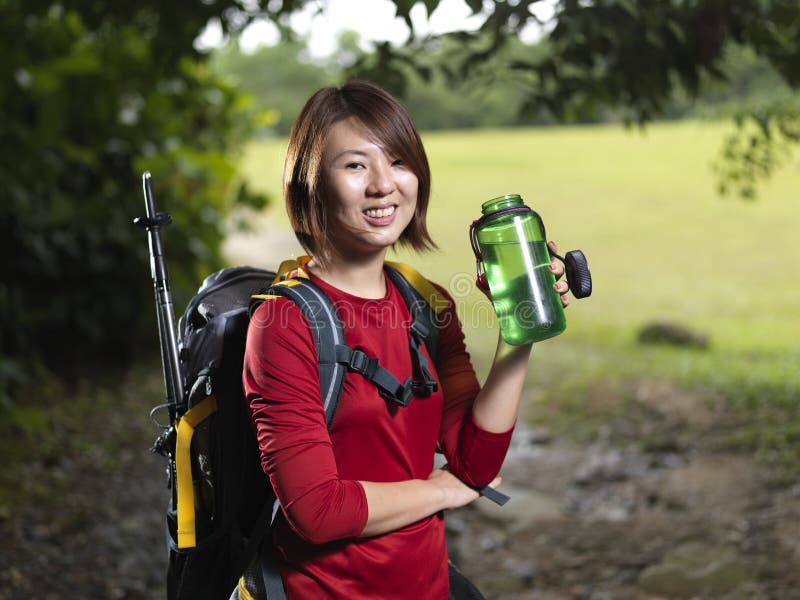 Water replenishment is vital as you do trekking. Here Asian Female hiker taking a rest and having water.