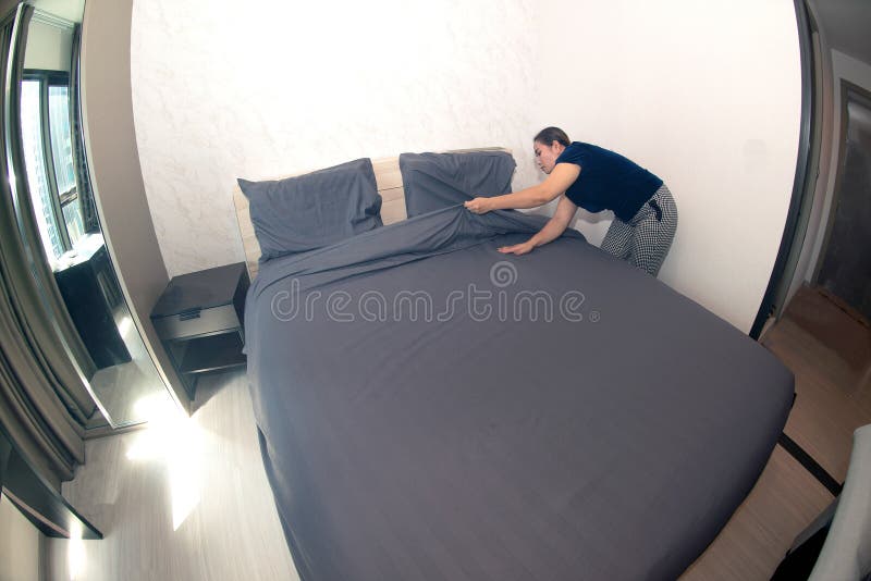 An Asian female maid making bed in hotel room. Housekeeper Making Bed.