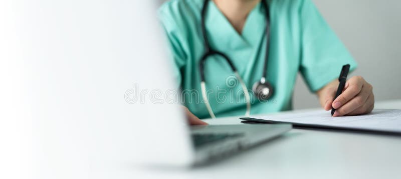 Asian female Nurse or Surgeon Doctor in green uniform working on laptop and writing something information of patient in paperwork