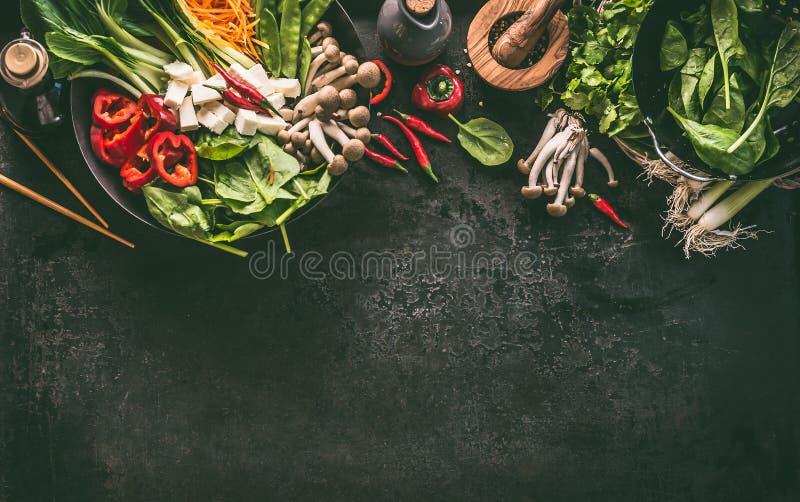 Asian food background. Wok pan with vegetarian ingredients: vegetables and tofu on kitchen table with chopsticks, herbs and spices