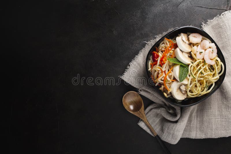 Asian food made with noodles, mushrooms, and vegetables on a black surface with copy space. A closeup shot of asian food made with noodles, mushrooms, and