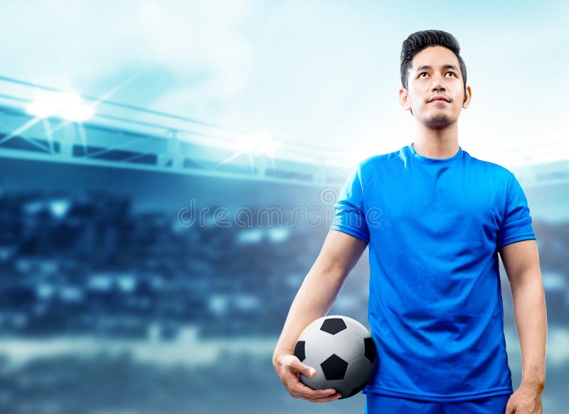 Asian football player man in blue jersey holding the ball on the football field stock photos Asian football player man in blue jersey holding the ball on the football field stock photos