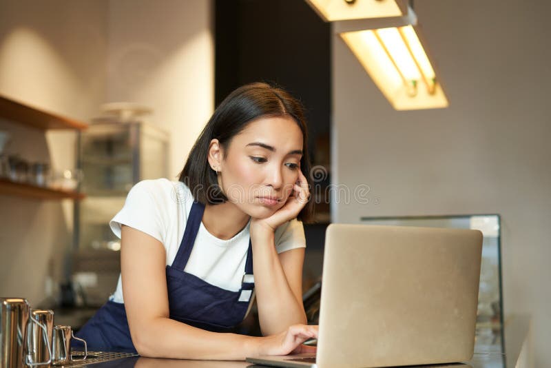 Asian Girl Barista Standing Behind Counter In Cafe Looking As At