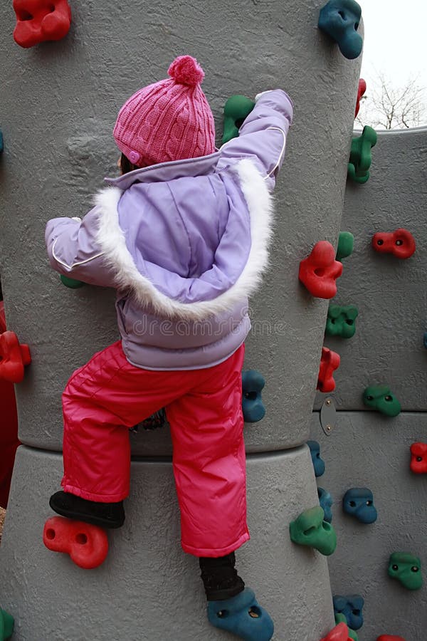 Asian girl bundled for winter climbing rock wall