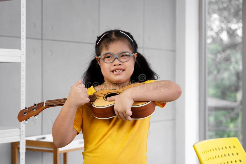 Asian girl with Down`s syndrome play ukulele.