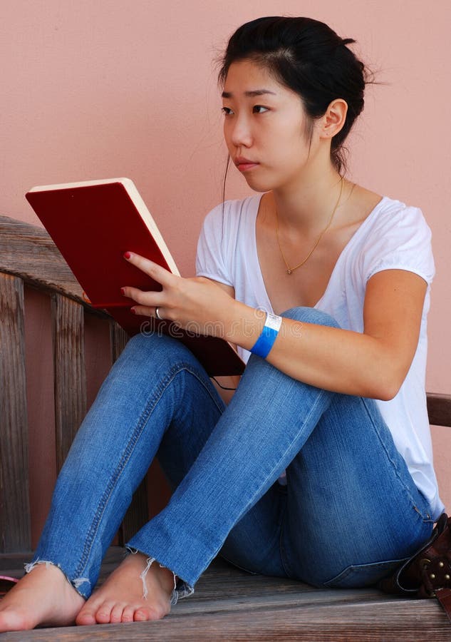 A young Asian woman drawing in a notepad while sitting on a bench. A young Asian woman drawing in a notepad while sitting on a bench.
