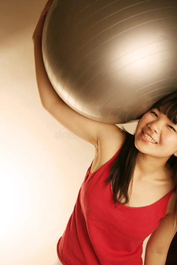 Asian girl holding exercise ball over her head