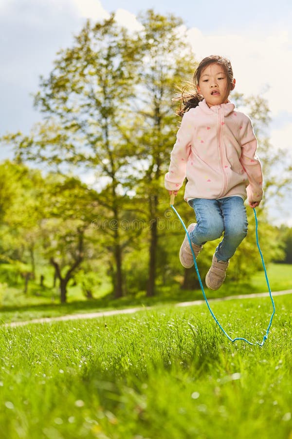 Asian girl is jumping rope in the park on a meadow in summer vacation