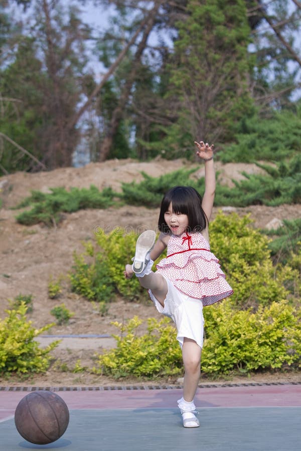 La ragazza asiatica a calci un pallone da basket con grande divertimento.