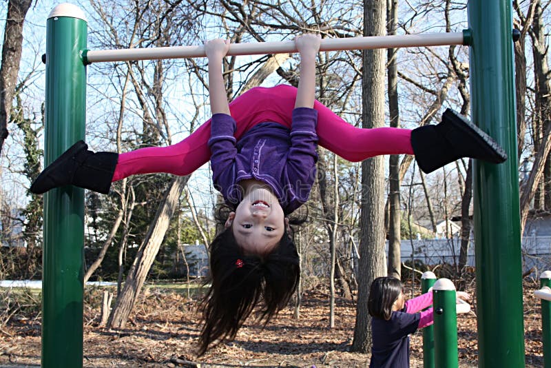 Little asian girl hanging onto bars upside down and holding on to bars.