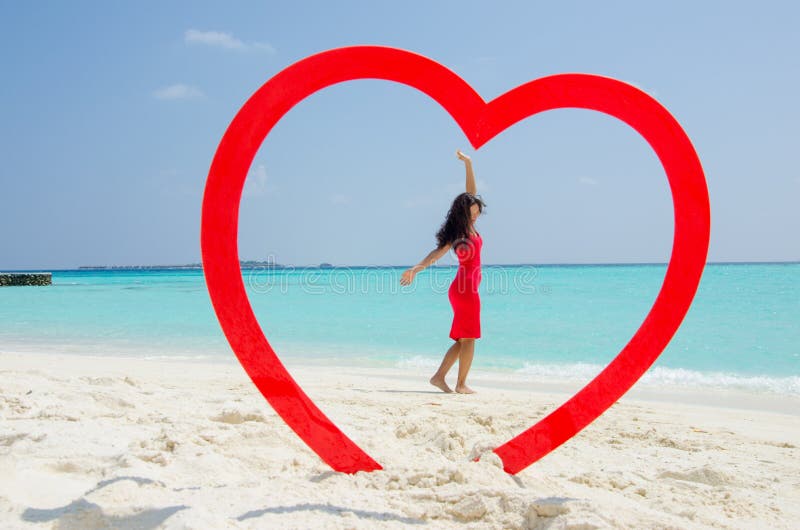 Asian girl in a red dress rising hands at the tropical beach inside heart stock photography Asian girl in a red dress rising hands at the tropical beach inside heart stock photography
