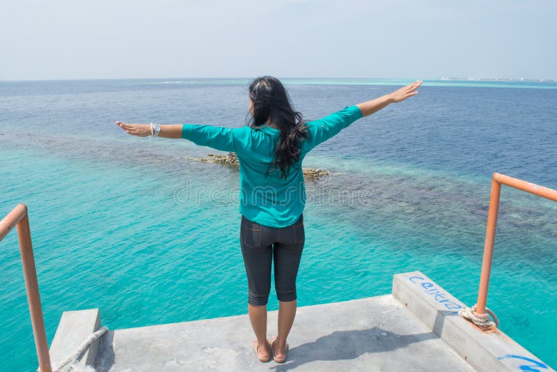 Asian girl standing at the top facing ocean and rising hands