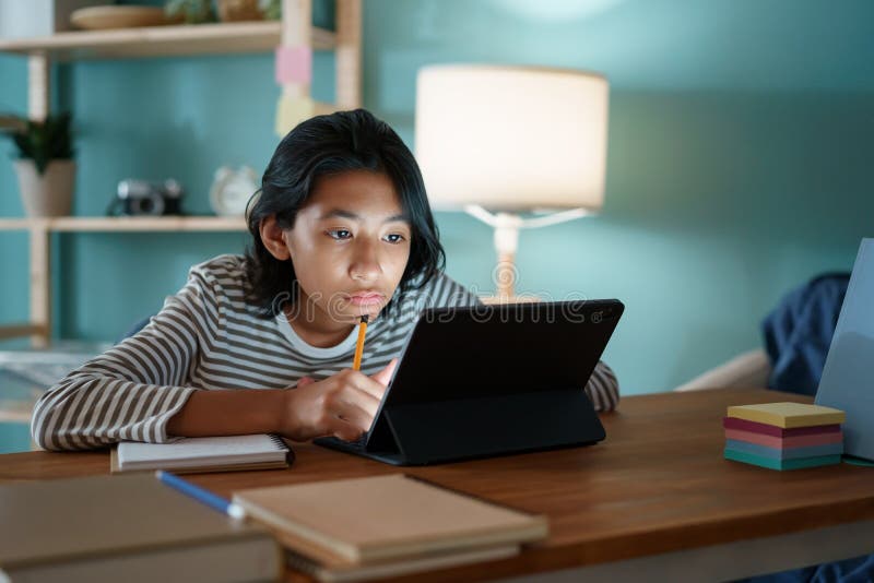 Education. Asian girl is studying online via the internet on tablet while sitting on a desk at home night. Concept of online learn. Ing at home royalty free stock images Education. Asian girl is studying online via the internet on tablet while sitting on a desk at home night. Concept of online learn. Ing at home royalty free stock images
