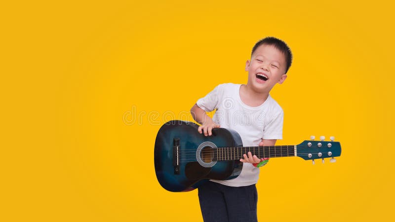 Asian happy smiling boy having fun playing guitar isolated on colored background, Music for kids and toddlers concept. Asian happy smiling 5 years old boy having stock photo