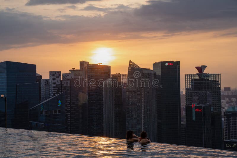 Asian holiday makers enjoying the scenic sunset view of Marina Bay and Singapore business district form the comfort on roof top po royalty free stock photography Asian holiday makers enjoying the scenic sunset view of Marina Bay and Singapore business district form the comfort on roof top po royalty free stock photography