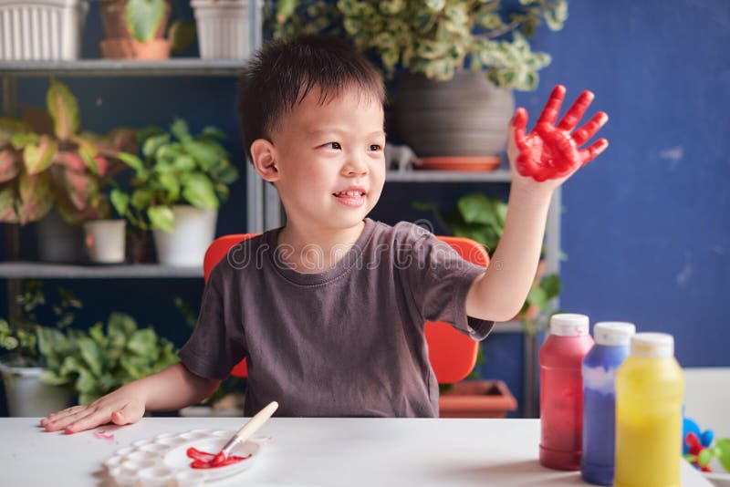 Asian kindergarten boy finger painting with hands and watercolors, kid having fun painting at home, Creative play for kids and