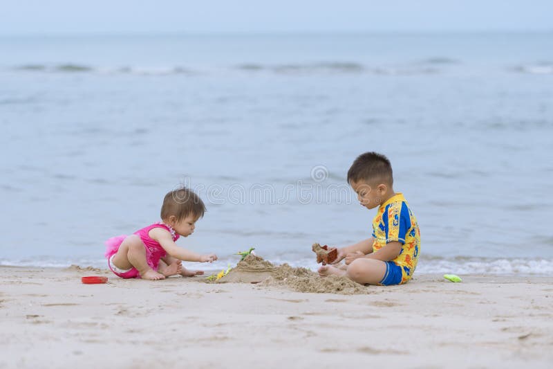 Asian little boy and his baby sister playing together on the sandy beach.