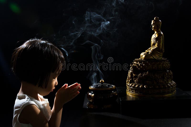 Asian Little Chinese Girl Praying in front of Buddha in isolated Black Background