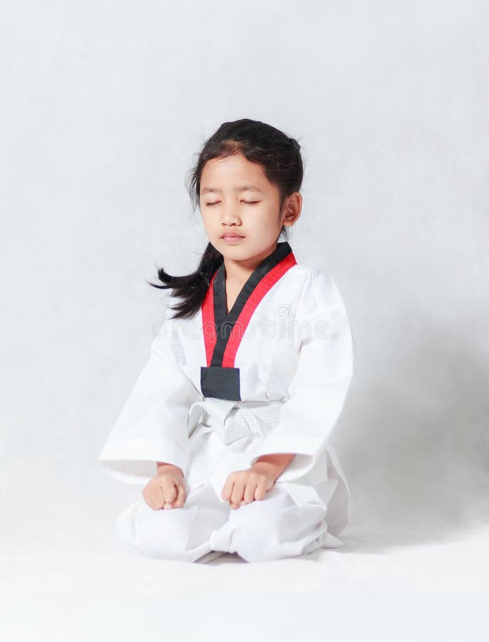 Asian little girl is sitting for concentration in taekwondo uniform on white background