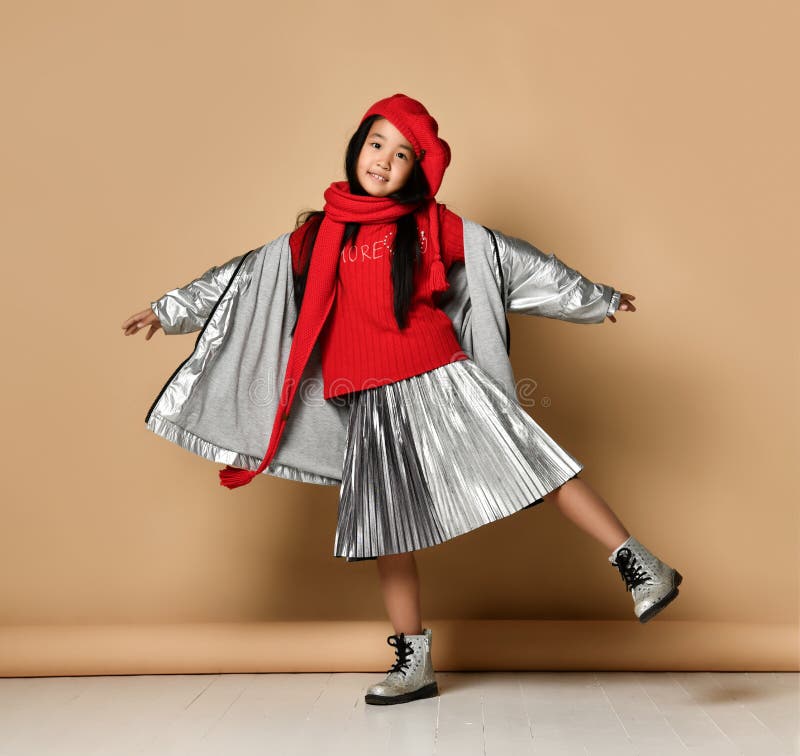 Asian little model girl wearing red beret, scarf, sweater and silver skirt and jacket having fun.