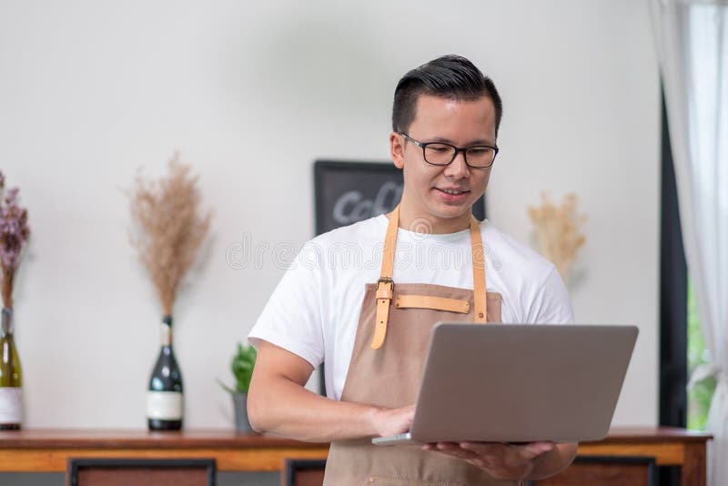Asian male Barista cafe owner using laptop checking stock business inside coffee shop, food and drink business start up royalty free stock image Asian male Barista cafe owner using laptop checking stock business inside coffee shop, food and drink business start up royalty free stock image