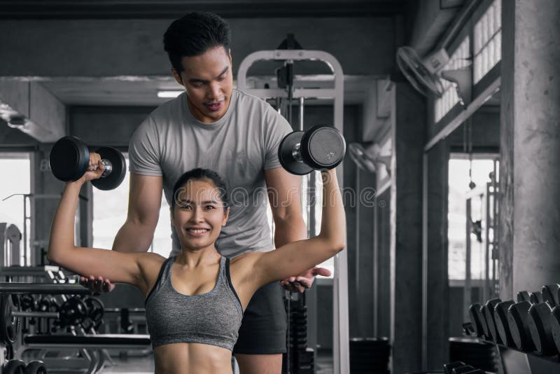 Male trainer training female working out with dumbbells wieght lifting in gym