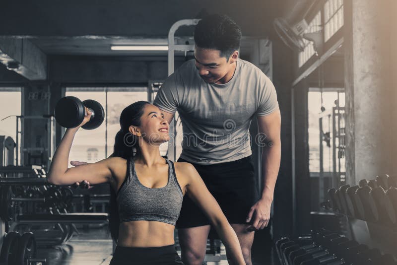 Male trainer training female working out with dumbbells wieght lifting in gym