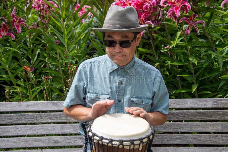 An Asian Man Sitting on a Bench Playing the Djembe. Stock Image Image