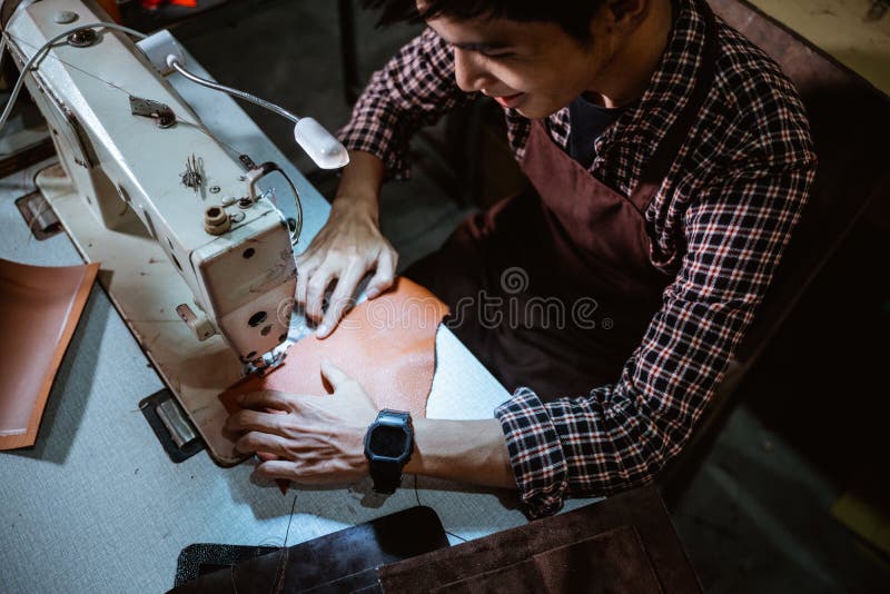 Asiático hombre sastre de coser piel de coser máquina mesa lámpara sobre el de coser estación.