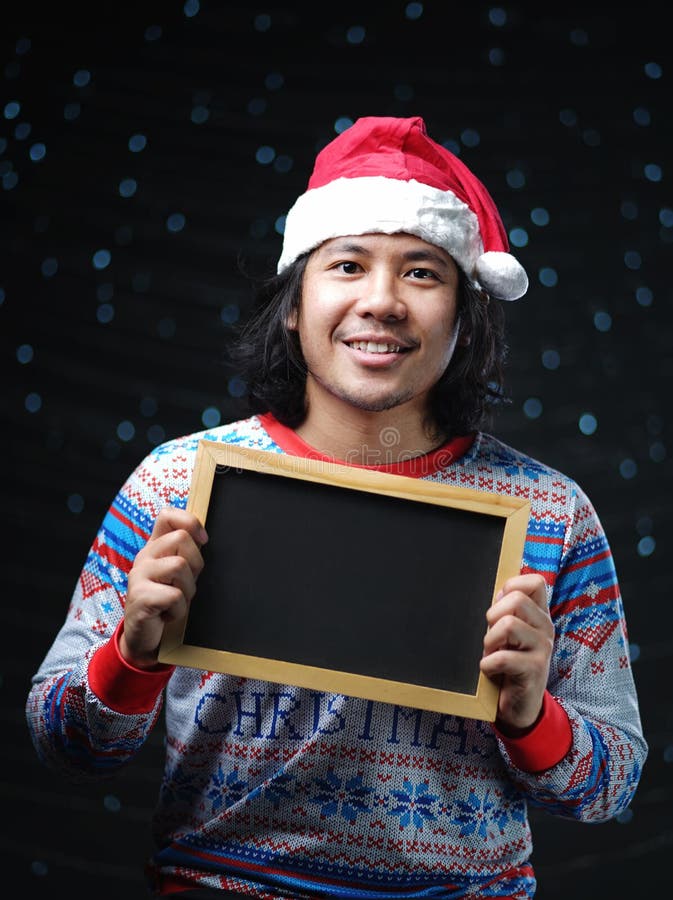 Asian Man Wearing Santa Hat and Christmas Sweater Holding Blackboard royalty free stock photo Asian Man Wearing Santa Hat and Christmas Sweater Holding Blackboard royalty free stock photo