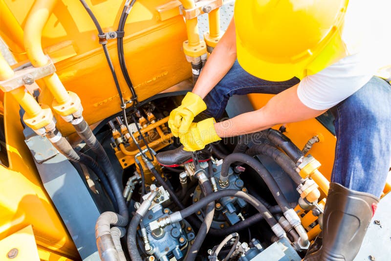 Asian motor mechanic working on construction or mining machinery in vehicle workshop. Asian motor mechanic working on construction or mining machinery in vehicle workshop