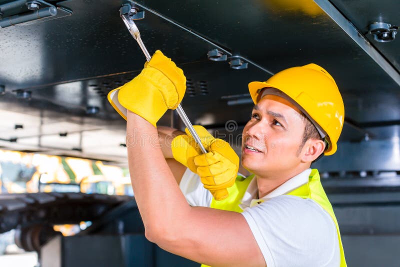 Asian motor mechanic working on construction or mining machinery in vehicle workshop. Asian motor mechanic working on construction or mining machinery in vehicle workshop