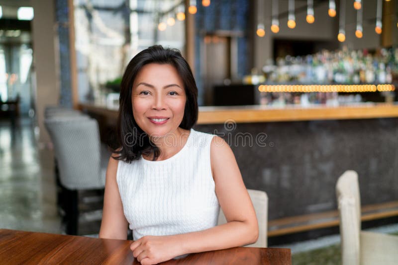 Asian middle age business woman smiling portrait. Happy elegant mature Chinese businesswoman lady in fancy restaurant