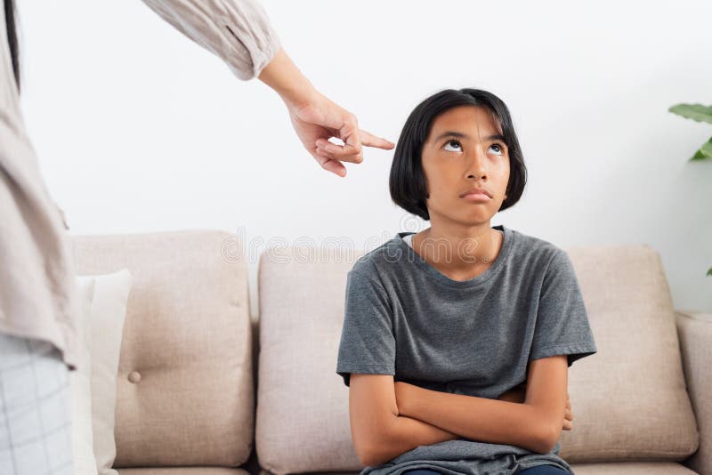 Asian mother is angry and scold her daughter while sitting on the sofa because of bad behavior. The concept of domestic violence