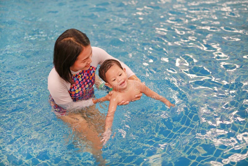 Asian mother take little Asian baby boy in swimming class. Happy toddler enjoying swim in pool with mom