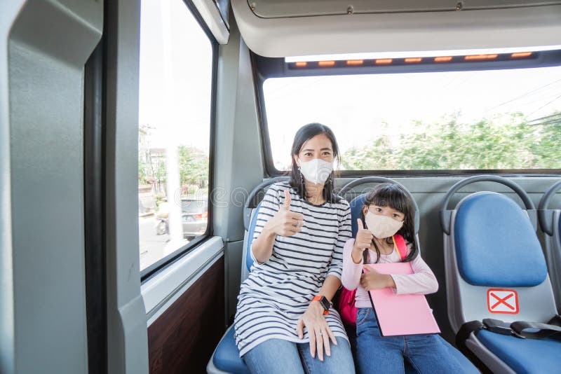 Asian mother taking her daughter to school by riding bus public transport wearing a face mask stock photo Asian mother taking her daughter to school by riding bus public transport wearing a face mask stock photo