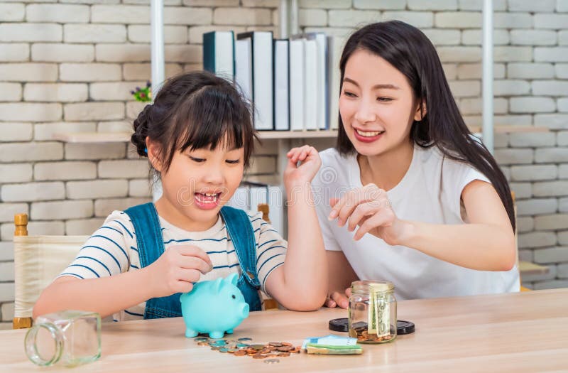 Asian mother teaching her daughter about financial saving and money management using piggy bank and saving jar