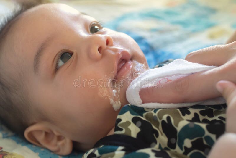 Asian mother is wiping her baby`s face after infant baby boy vomiting with soft sunbeam. people and family lifestyle concept.