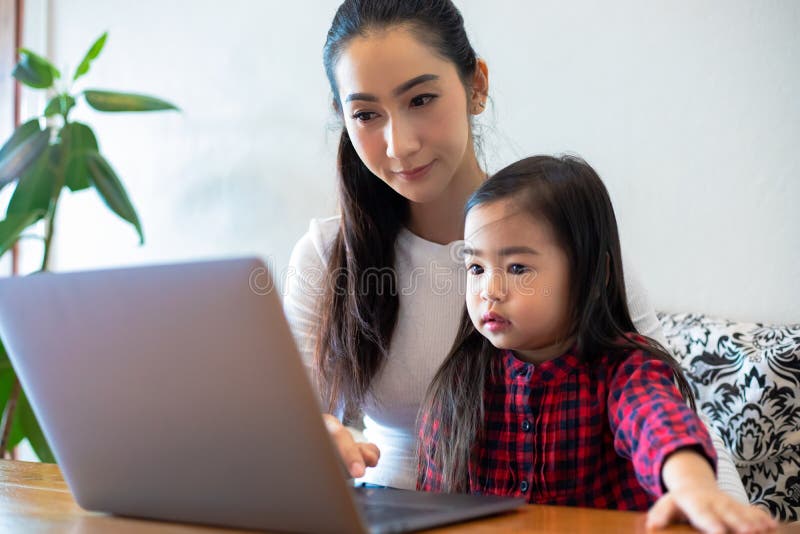 Asian mothers are teaching their daughters to read a book and use notebooks and technology for online learning during school