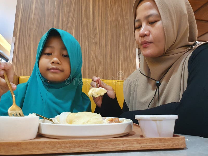 Asian muslim woman eating breakfast with her daughter at cafe, people eating food, happy parent and kid relation royalty free stock photography