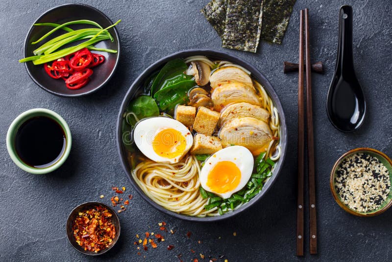 Asian noodle soup, ramen with chicken, tofu, vegetables and egg in black bowl. Slate background. Top view. royalty free stock photo Asian noodle soup, ramen with chicken, tofu, vegetables and egg in black bowl. Slate background. Top view. royalty free stock photo