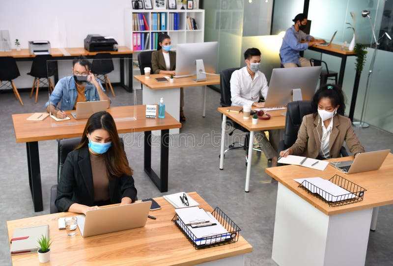 Asian office workers wearing face masks working in new normal office and doing social distancing