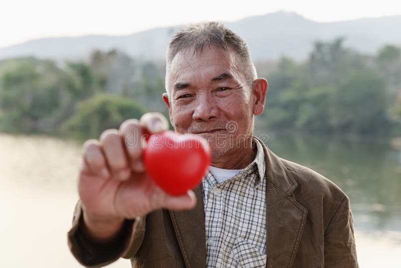 Asian old man smiling and showing red heart, valentine`s day and senior healthy concept